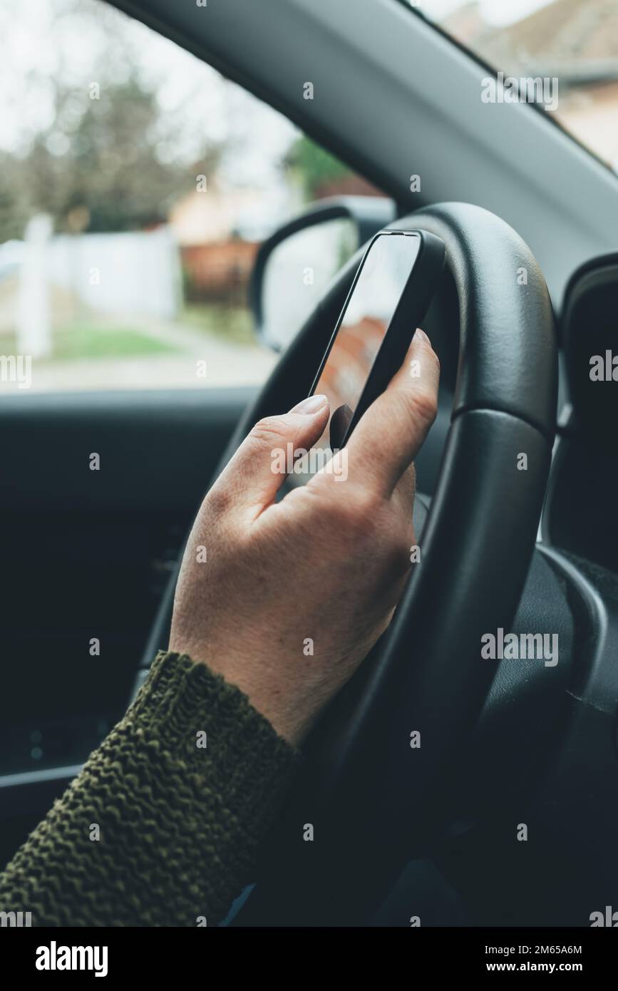 Closeup shot of female hand typing message on smartphone device, casual woman driver wearing green knitted sweater using mobile phone in vehicle inter Stock Photo