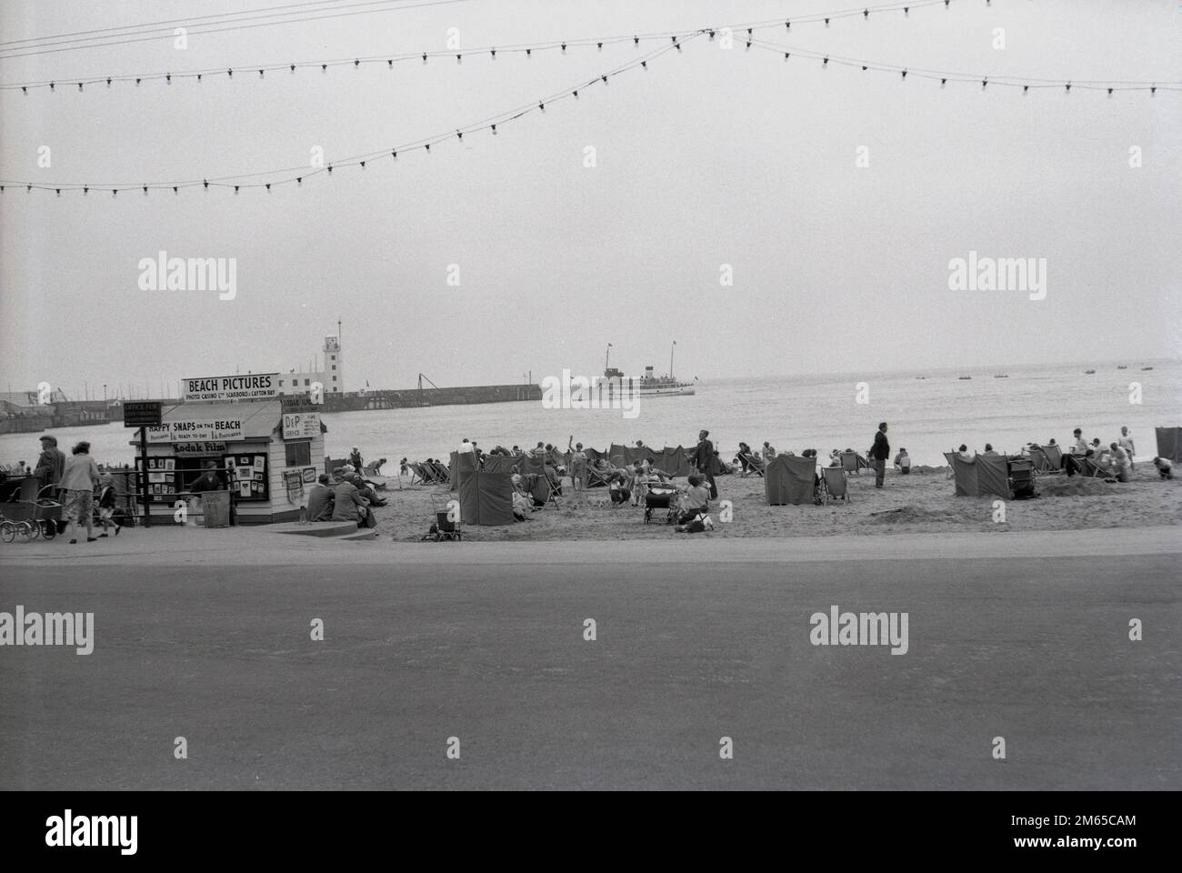 1950s, historical, people at the beach at North bay on Scarborough, a seaside resort in East Yorkshire, England, UK. A kiosk there 'Beach Pictures' offers Happy Snaps on the Beach produced by Photo Casino Ltd of Scarborough & Clayton Bay. The coastal town grew to be a major seaside destination and by many photographic studios were set up to provide holiday pictures for the visitors, including after WWII, Photo Casino Co Ltd. Stock Photo