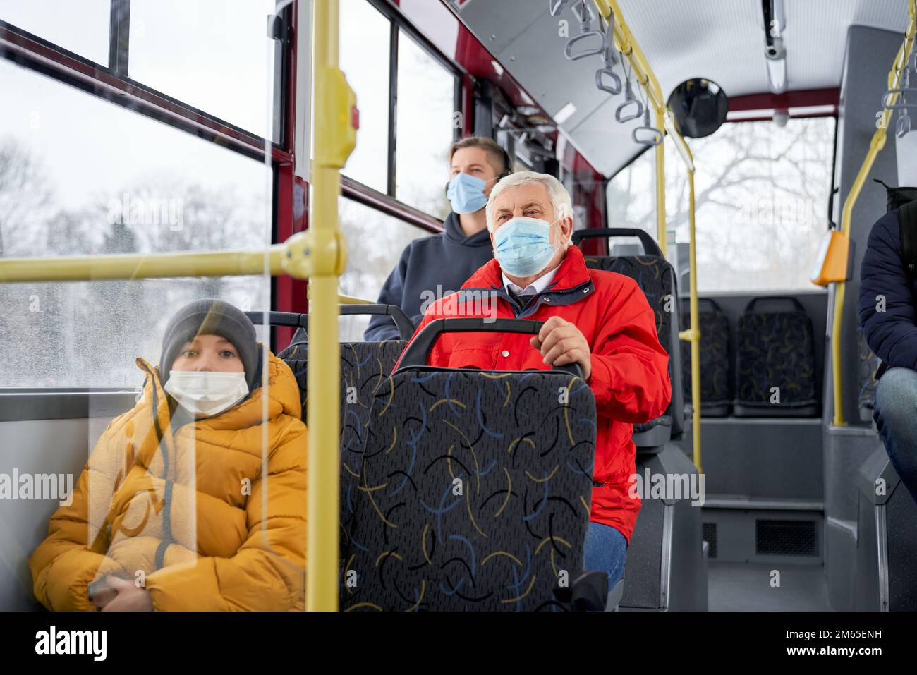 Front view of passengers sitting on bus, wearing medical masks, protecting from global pandemic. People traveling by public transport, looking forward Stock Photo