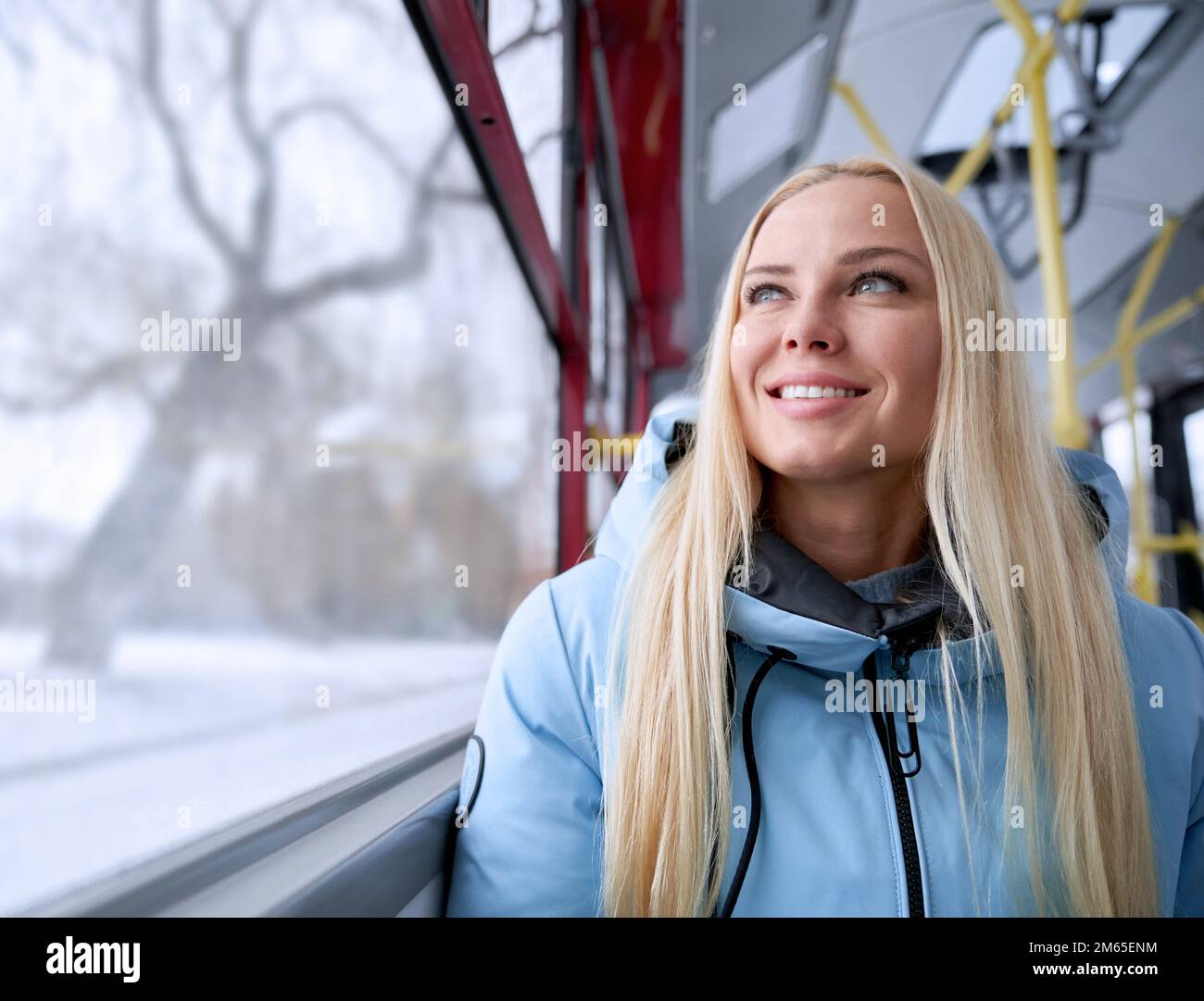 Front view of beautiful blonde woman going home from work by bus in cold winter weather, happy, glad. Pretty young woman sitting, smiling, looking up. Stock Photo