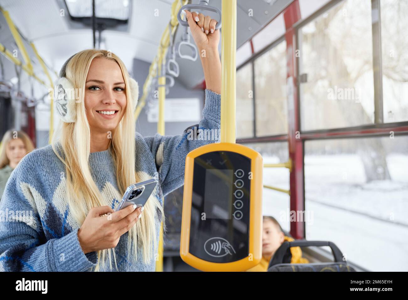 Portrait of fair long haired pretty female smiling nicely and looking directly in camera holding smarphone in one hand performing contactless payment Stock Photo