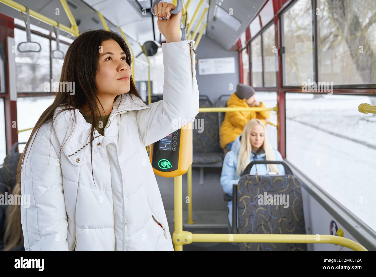 Portrait of cute nice female with long dark hair wearing white coat dreaming and thinking about future plans. Other passengers sitting staring at phon Stock Photo