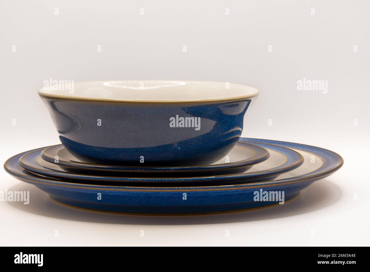 a centred bowl and three sizes of crockery plates in white with blue rims and edges and a gold trim Stock Photo