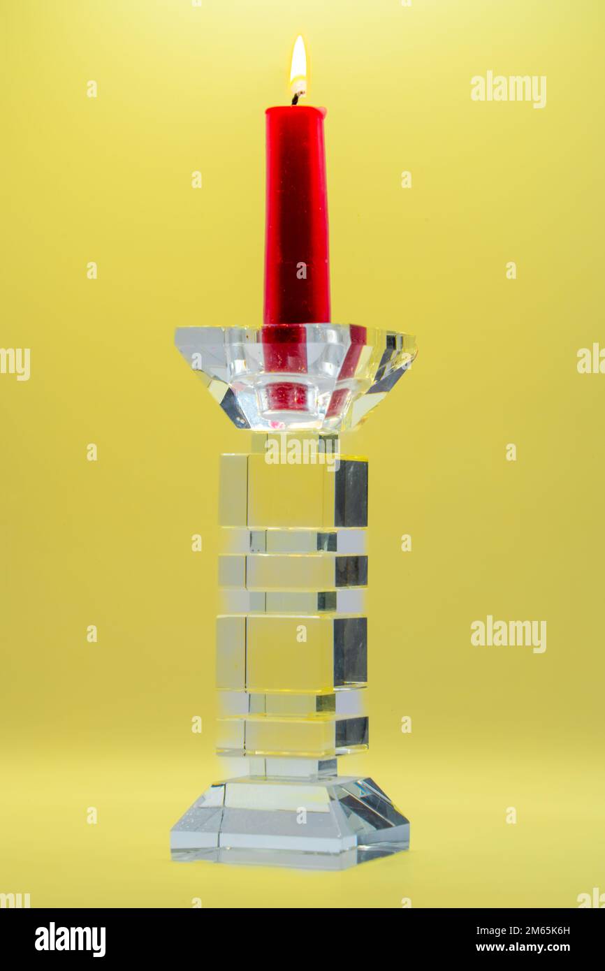 a red candle with burning orange yellow flame in clear glass sculptured
