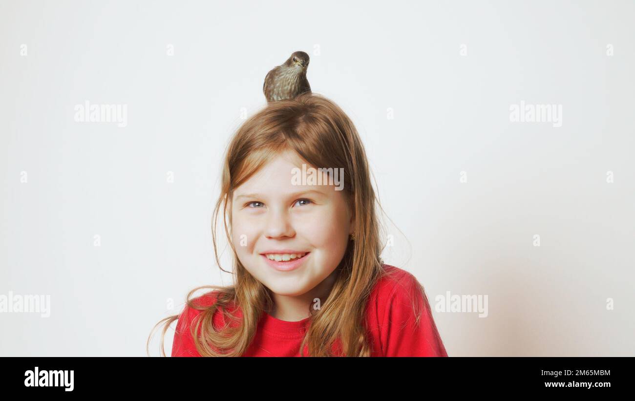 Grown up starling nestling sitting on head of glad little girl. Portrait of happy child on white