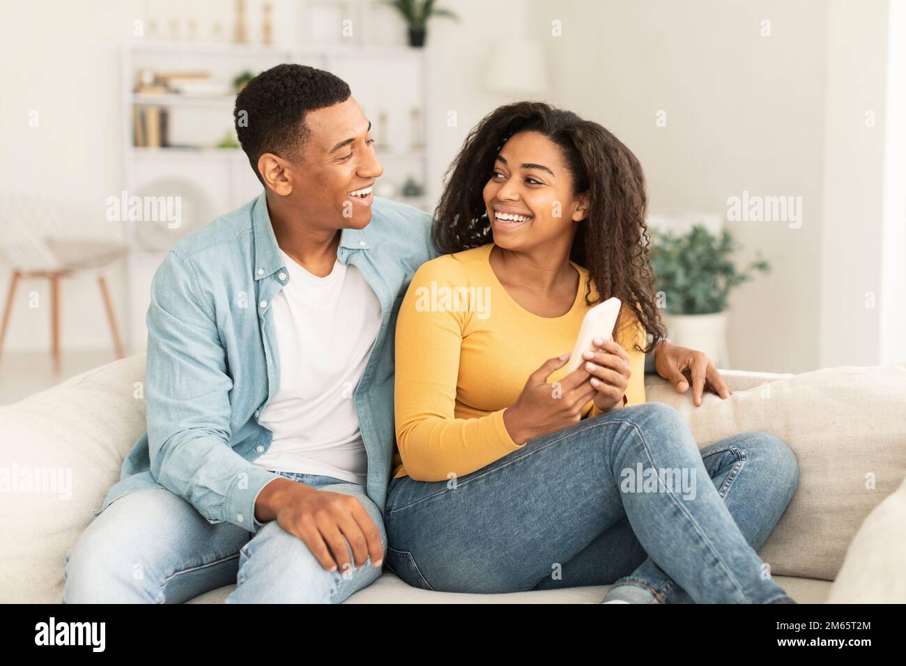 Cheerful millennial african american wife showing smartphone to husband