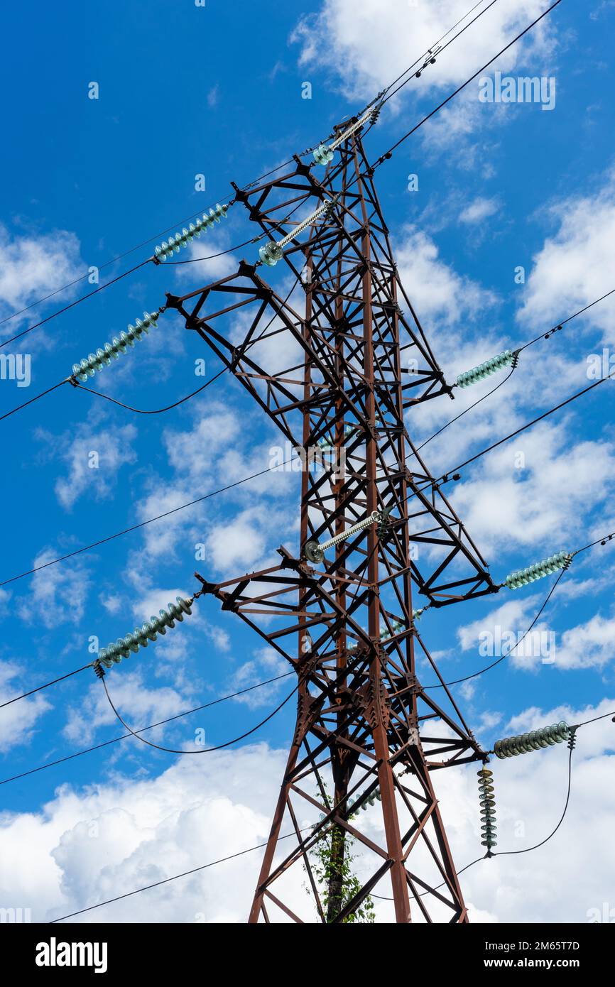 A pole of a high-voltage electric line on the background of a blue sky with white clouds Stock Photo