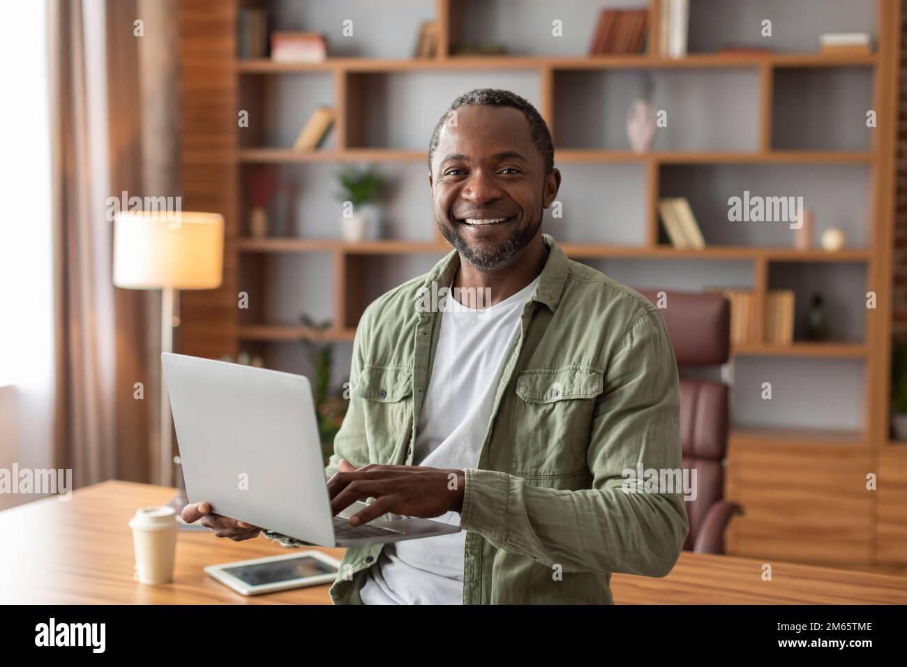 Smiling attractive mature black male manager with laptop work, make presentation and look at camera Stock Photo