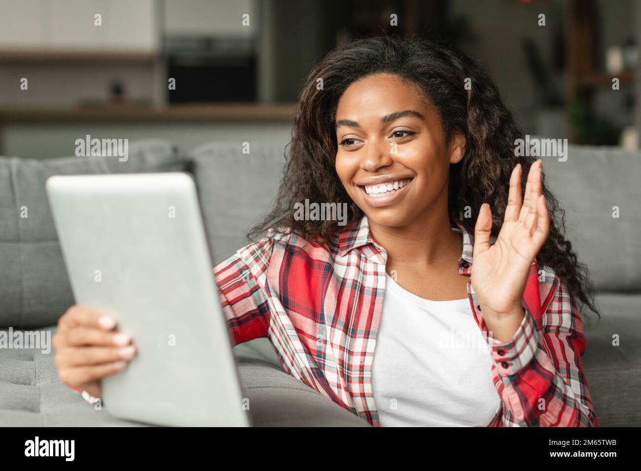 Glad millennial black lady blogger shoots video blog, has online call, makes greeting gesture in smartphone webcam Stock Photo