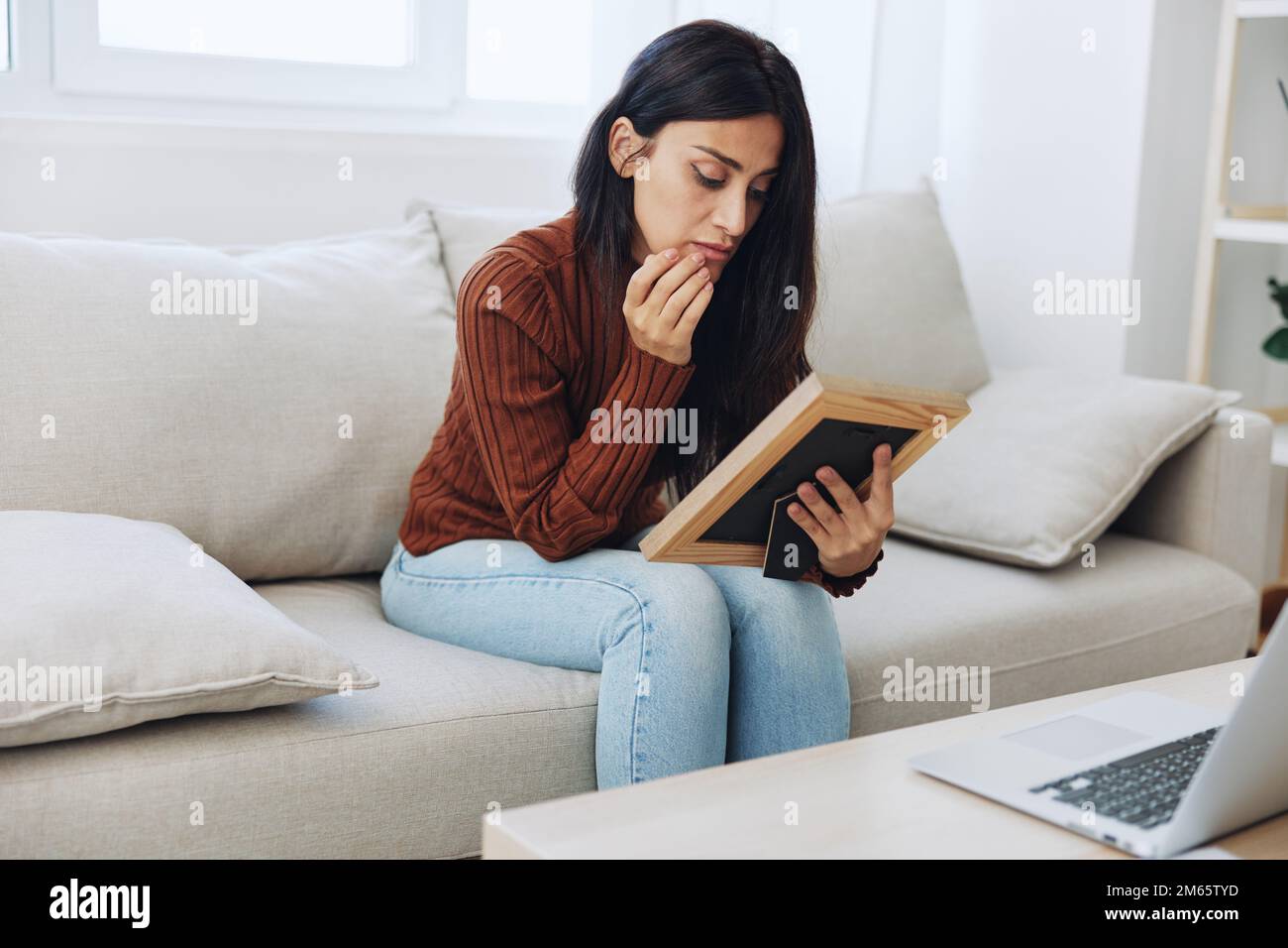 The woman looks sadly at the picture frames in her hands and with