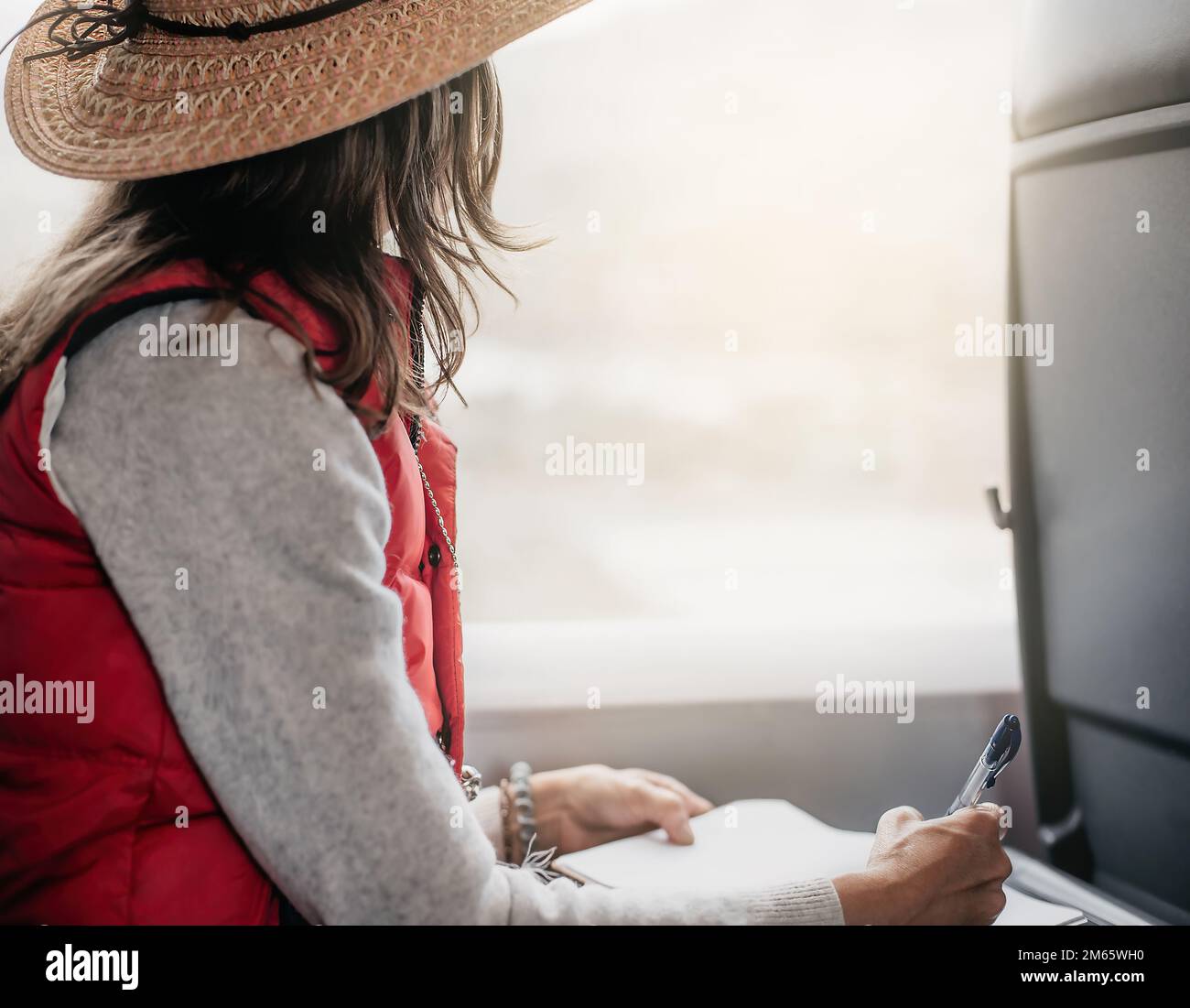 a woman in a hat sitting on a train while looking out the window and writing in a diary. Concept work and making the most of the time on a train Stock Photo