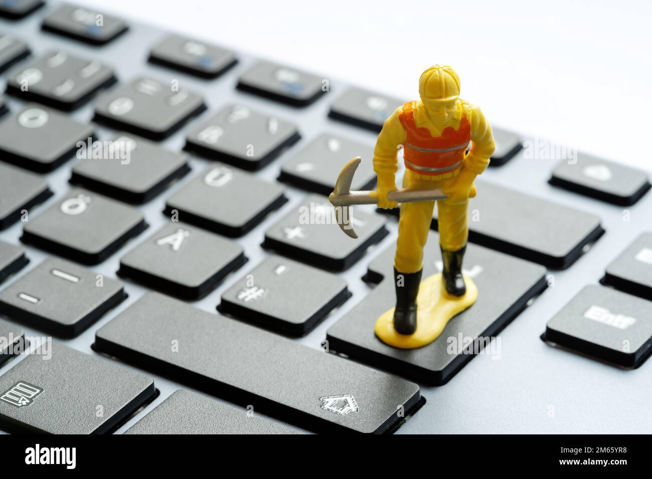 Construction worker figurine with a pickaxe standing on top of a simple desktop PC, computer keyboard. Data mining, crypto, cryptocurrency mining IT s Stock Photo