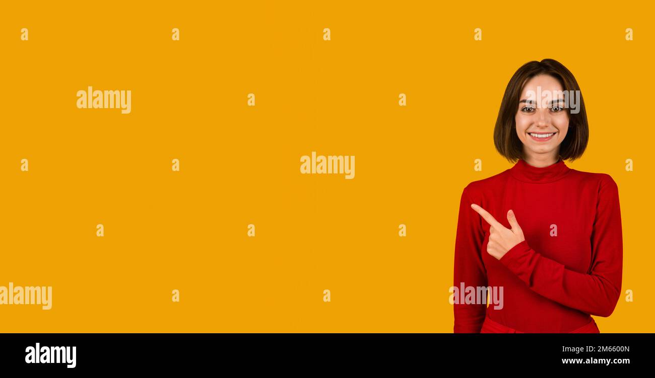 Happy beautiful young lady in red pointing at empty space Stock Photo