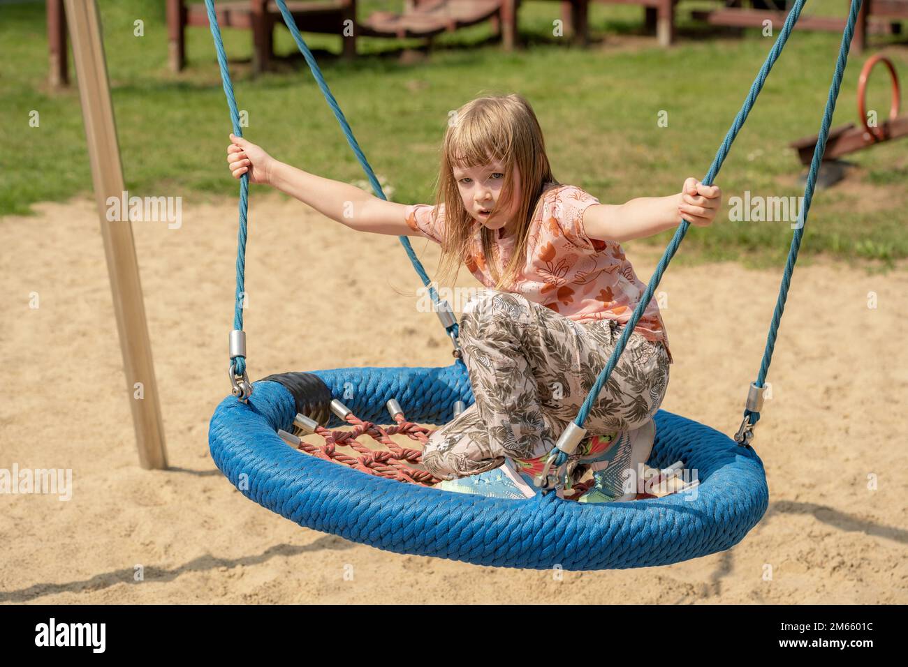 Happy elementary school age girl child swinging on a modern swing