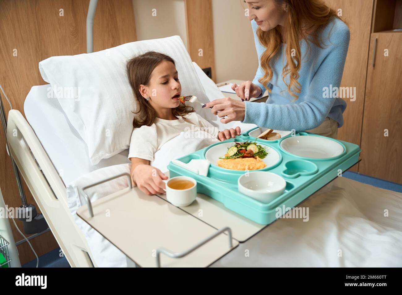 Caring mother feeds her daughter with dietary hospital food Stock Photo