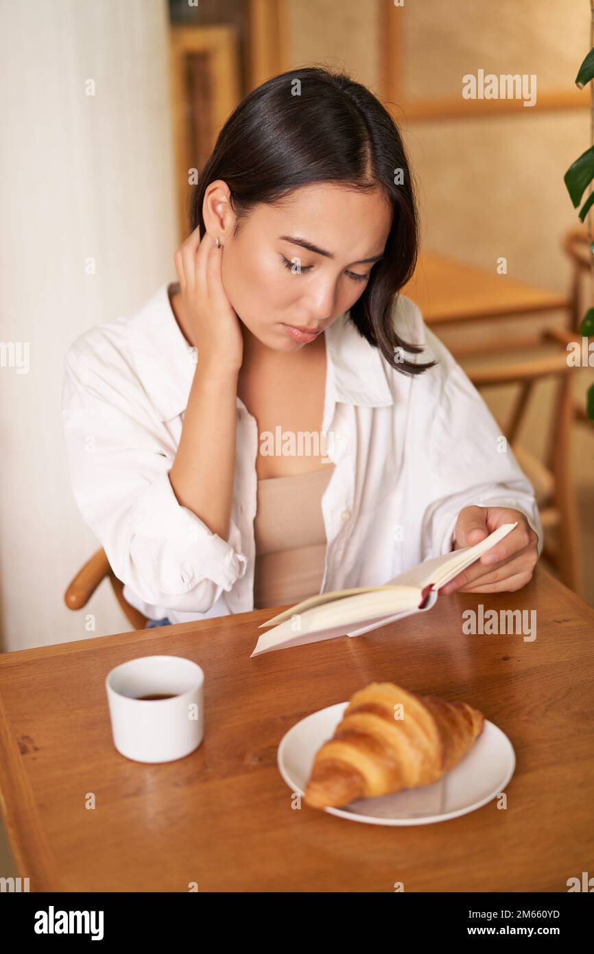 Asian girl reading book, looking sad, sitting in cafe and drinking ...