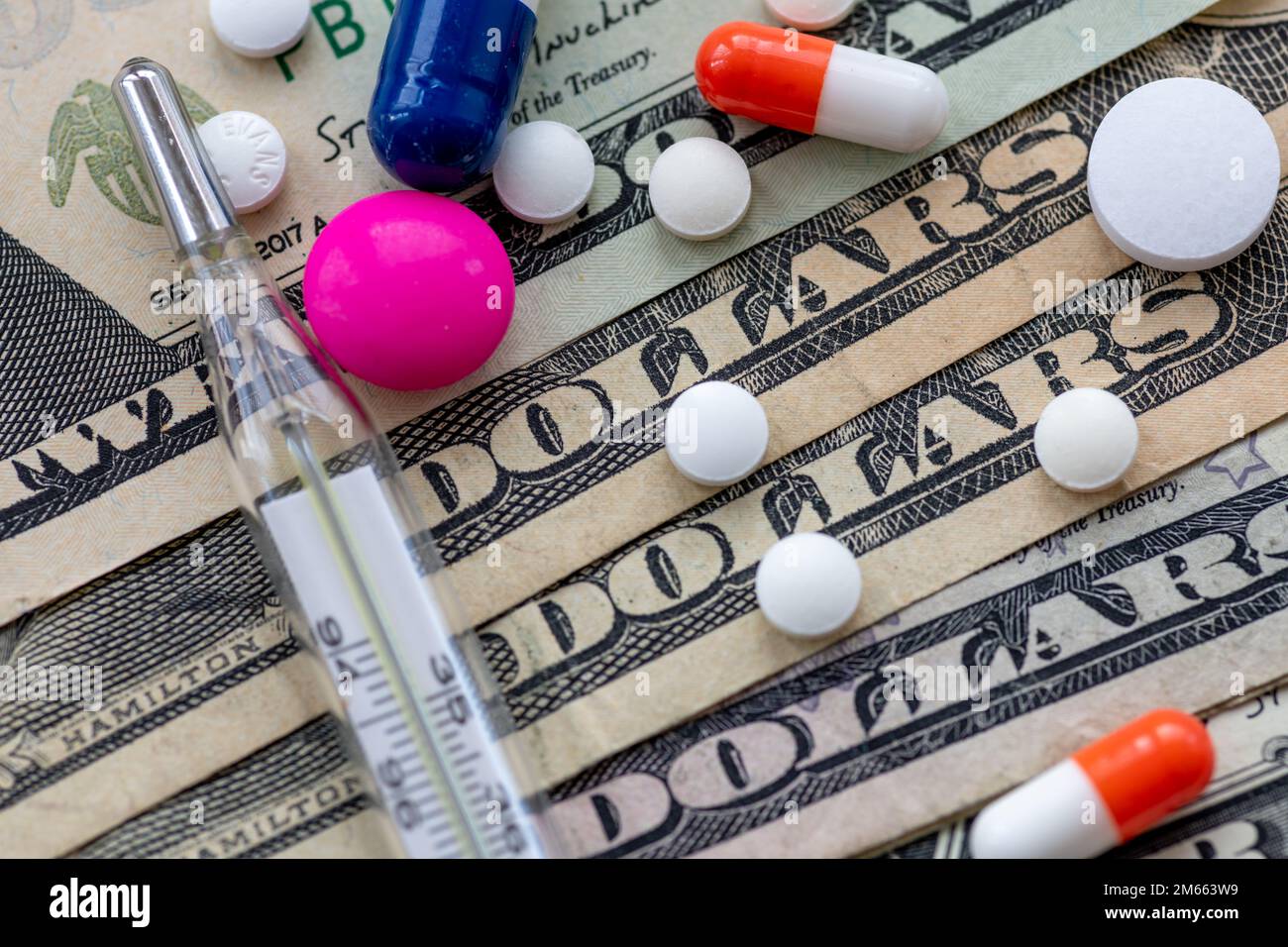 Close up of medicine and a thermometer on top of Dollar bills. Heath care cost, big pharma concept. Stock Photo