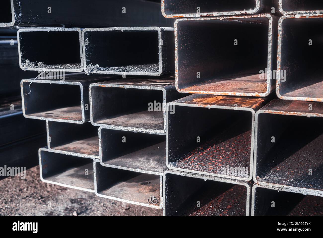 Stack of rolled steel products, metal pipes with rectangular cross-section, close-up photo with selective focus. Abstract heavy industry background ph Stock Photo