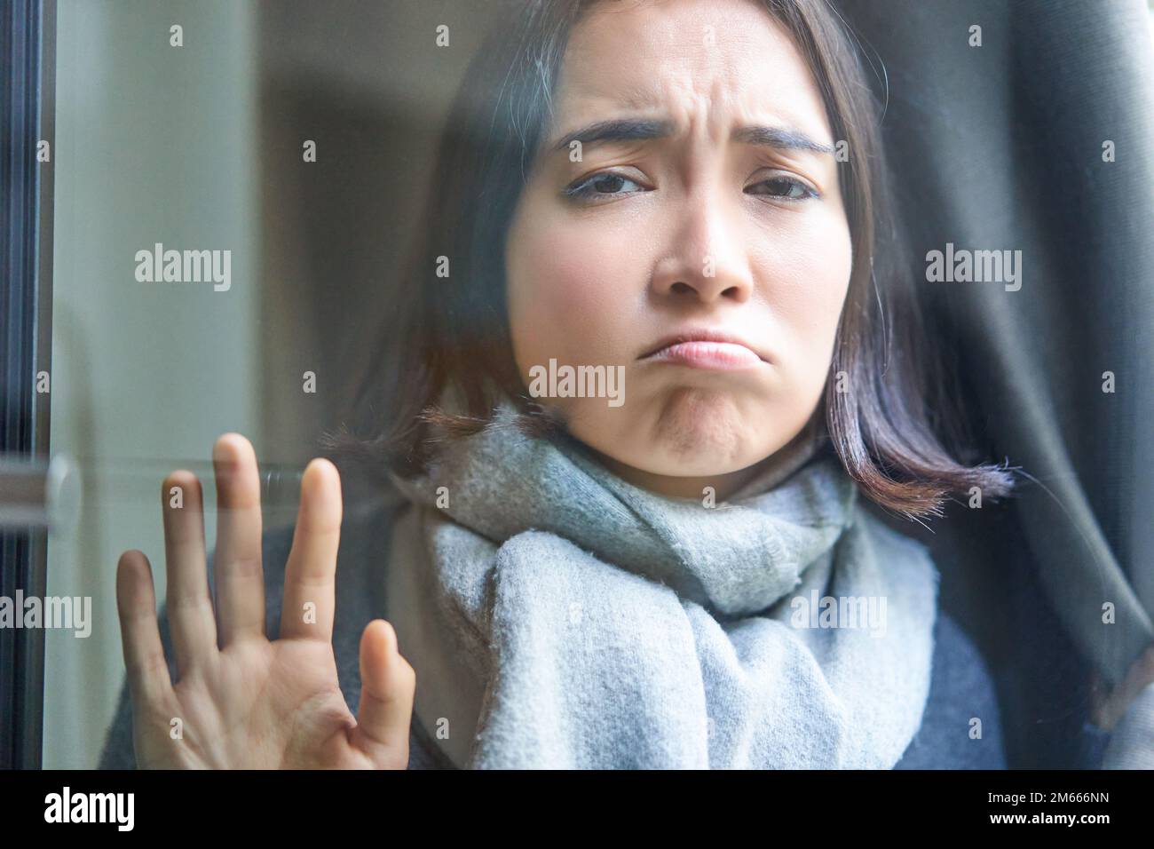 Portrait of sad ill woman staying at home, looking out of the window ...