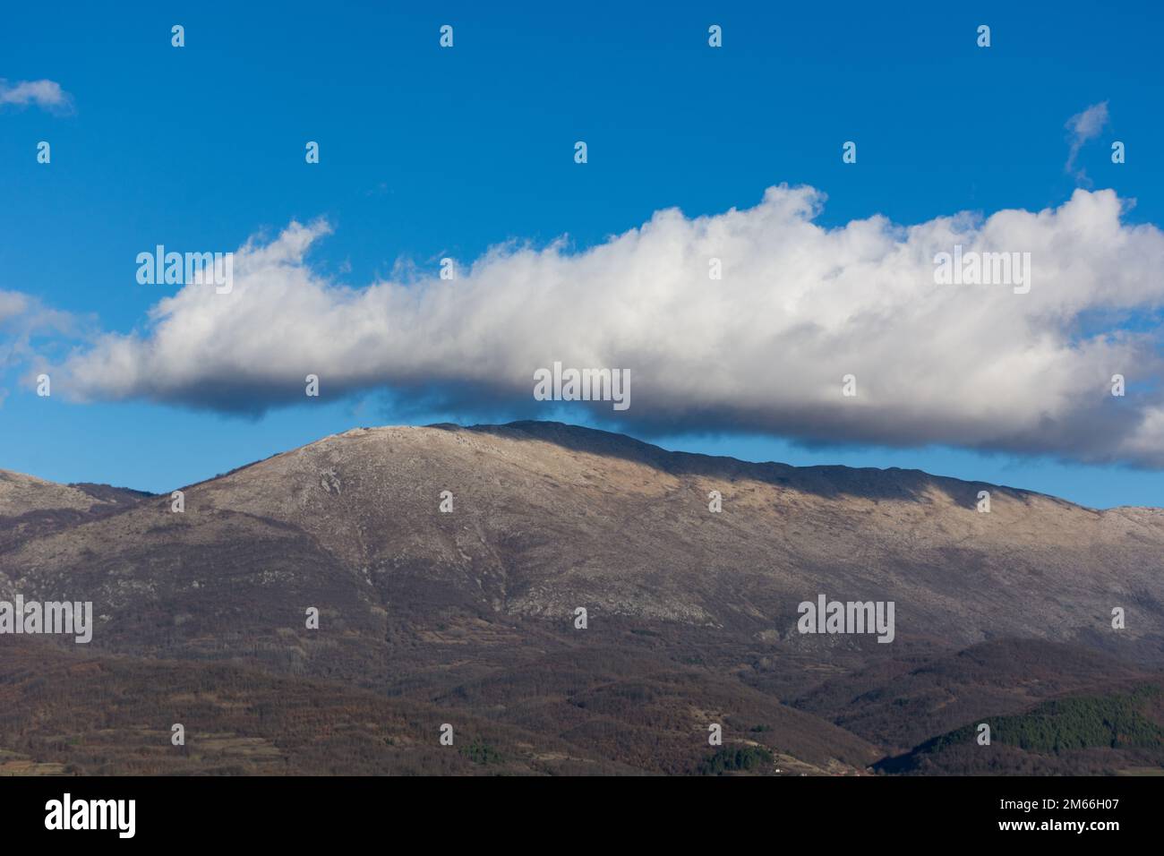 Gorgeous mountaintop view of Suva Planina with a white cloud almost touching it on a sunny day, this photo showcases the natural beauty of this place Stock Photo