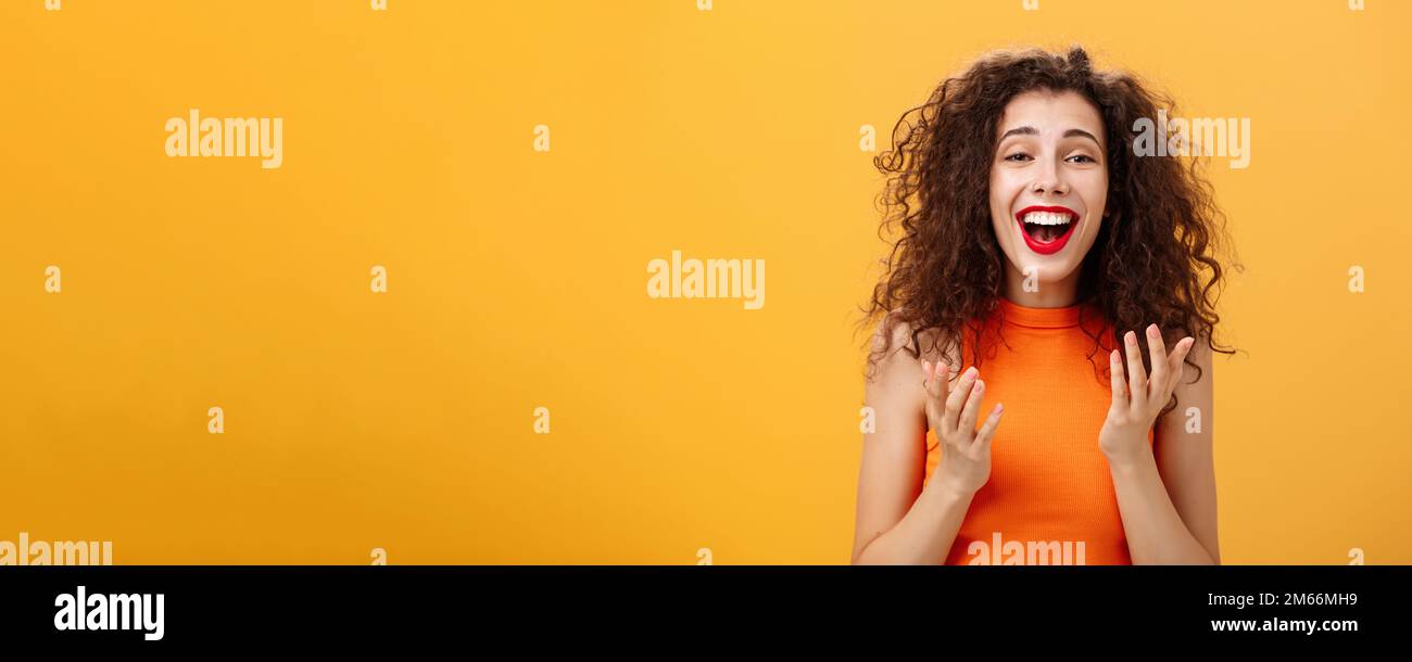 Surprised thrilled and joyful charming european female with curly hairstyle raising palms in grateful and delighted gesture smiling broadly hearing Stock Photo