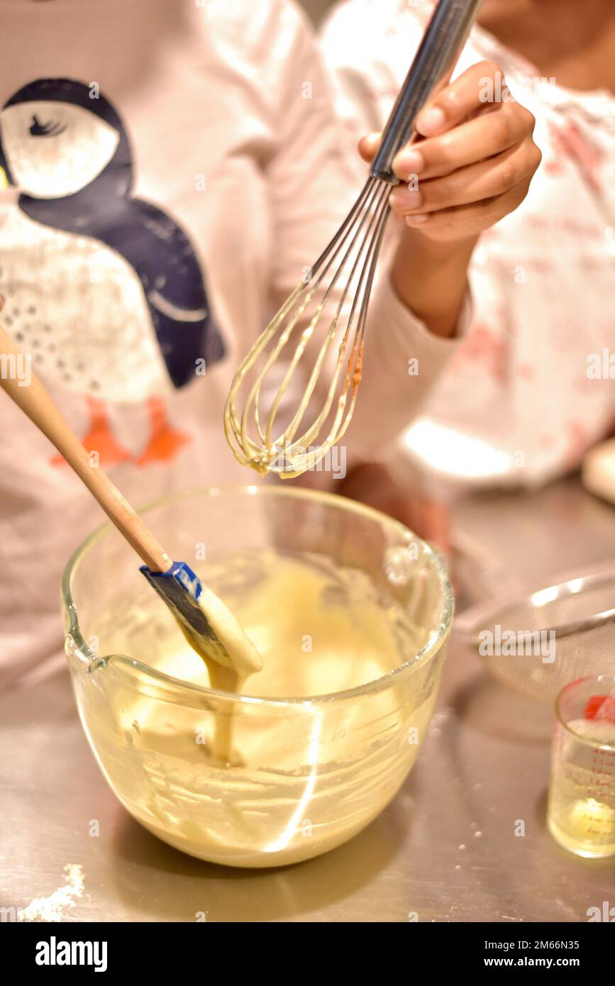 Kids holding a wire whisk and spatula mixing breakfast batter for