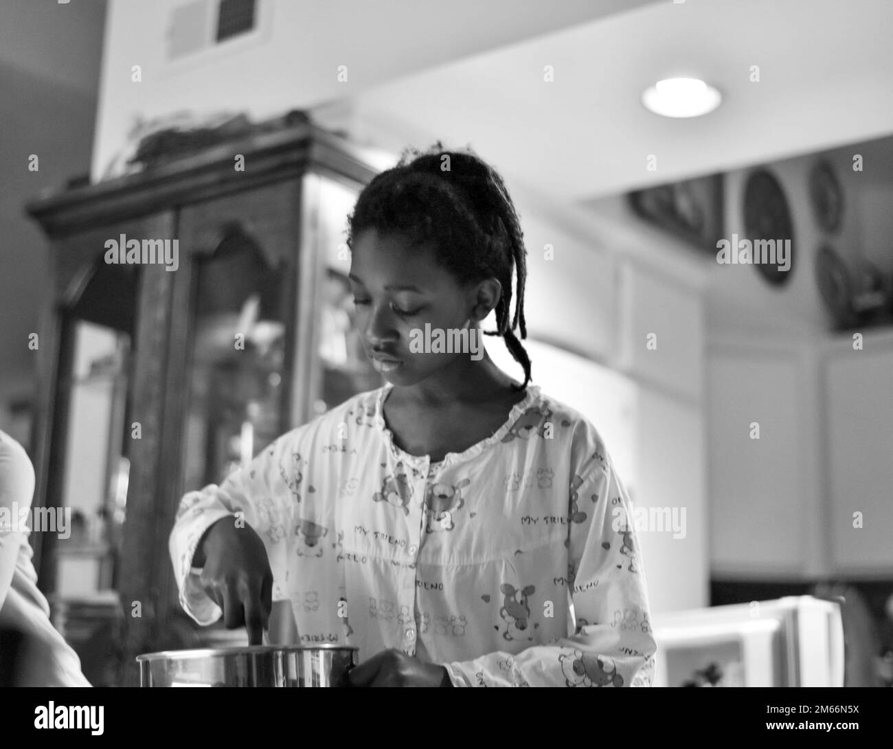 black and white photo of a young girl mixing breakfast ingredients in a shiny stainless steel bowl Stock Photo