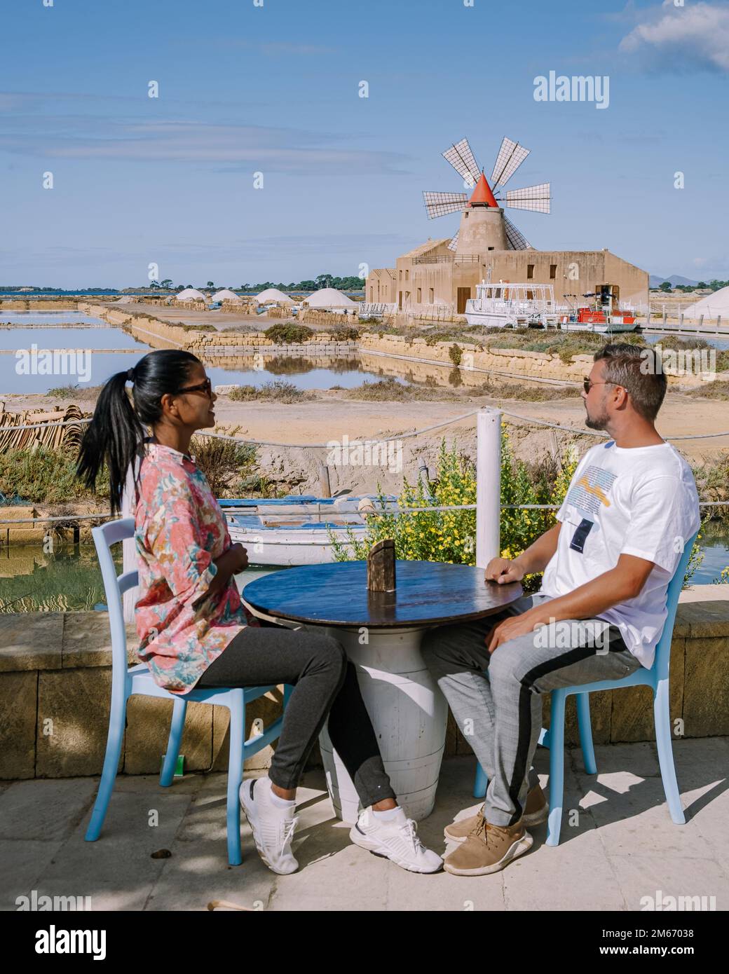 couple drinking coffee with a view at the Windmill and Salt Pans near Marsala, Sicily, Italy, Men and women on Vacation in Sicily Stock Photo