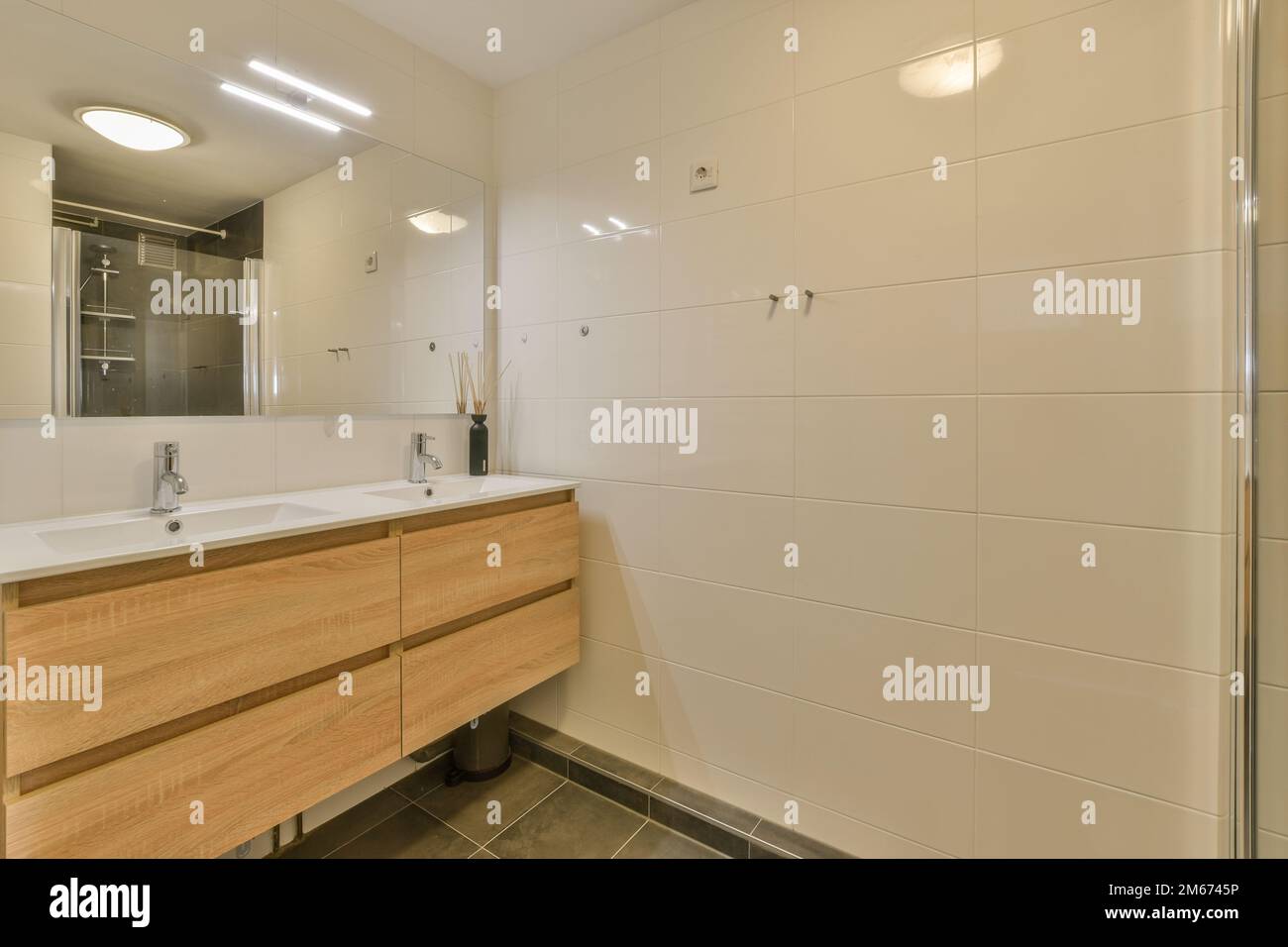 a modern bathroom with wood cabinets and white tiles on the walls, along with a large mirror in the corner Stock Photo