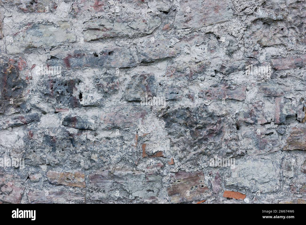Stone wall background closeup, horizontal plastered grunge red grey beige stonewall limestone pattern, old aged weathered gray lime plaster texture Stock Photo