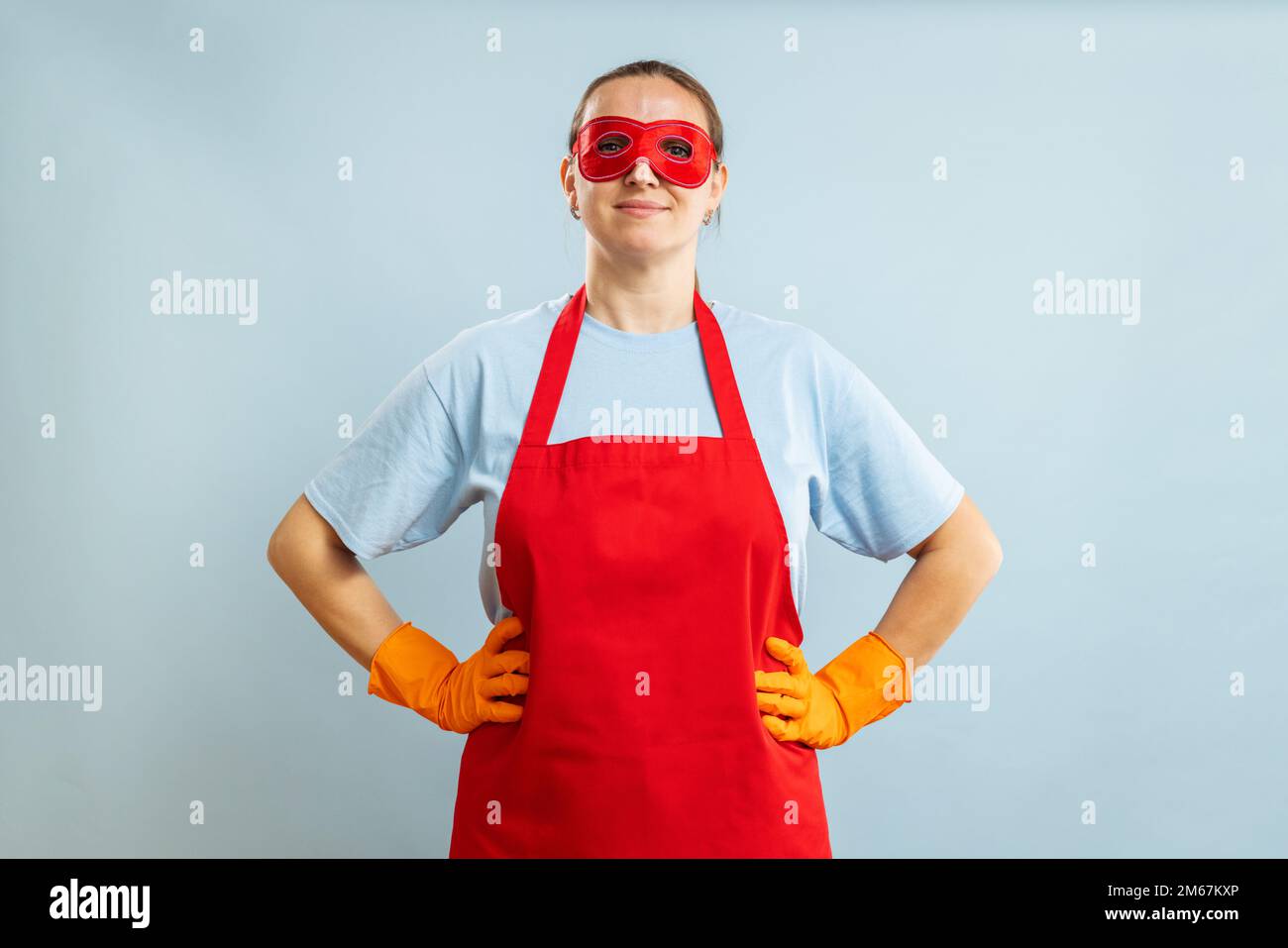 Young confident housewife in cleaning superhero costume on blue background Stock Photo