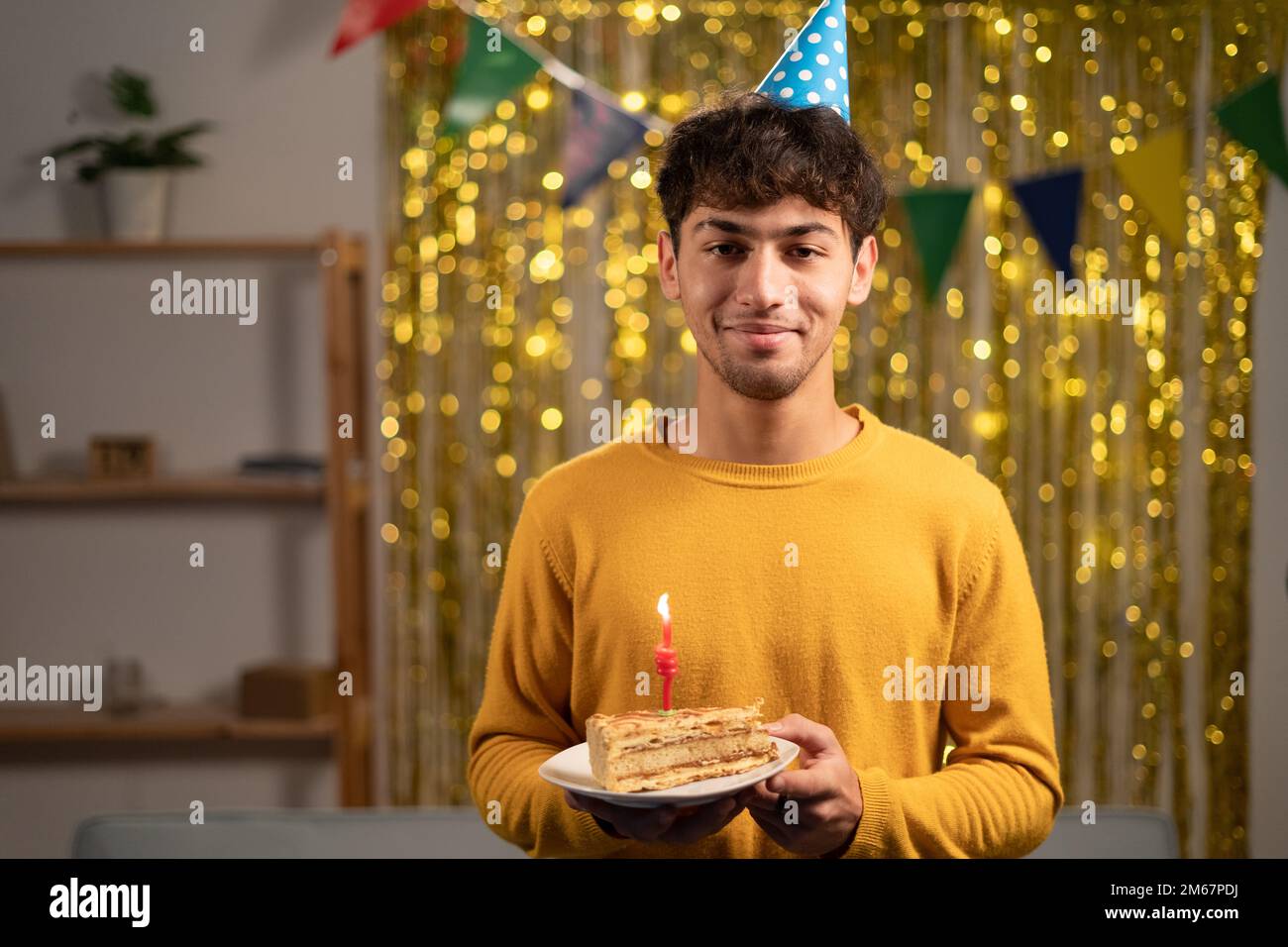 Young handsome man holding birthday sweet cake over golden home
