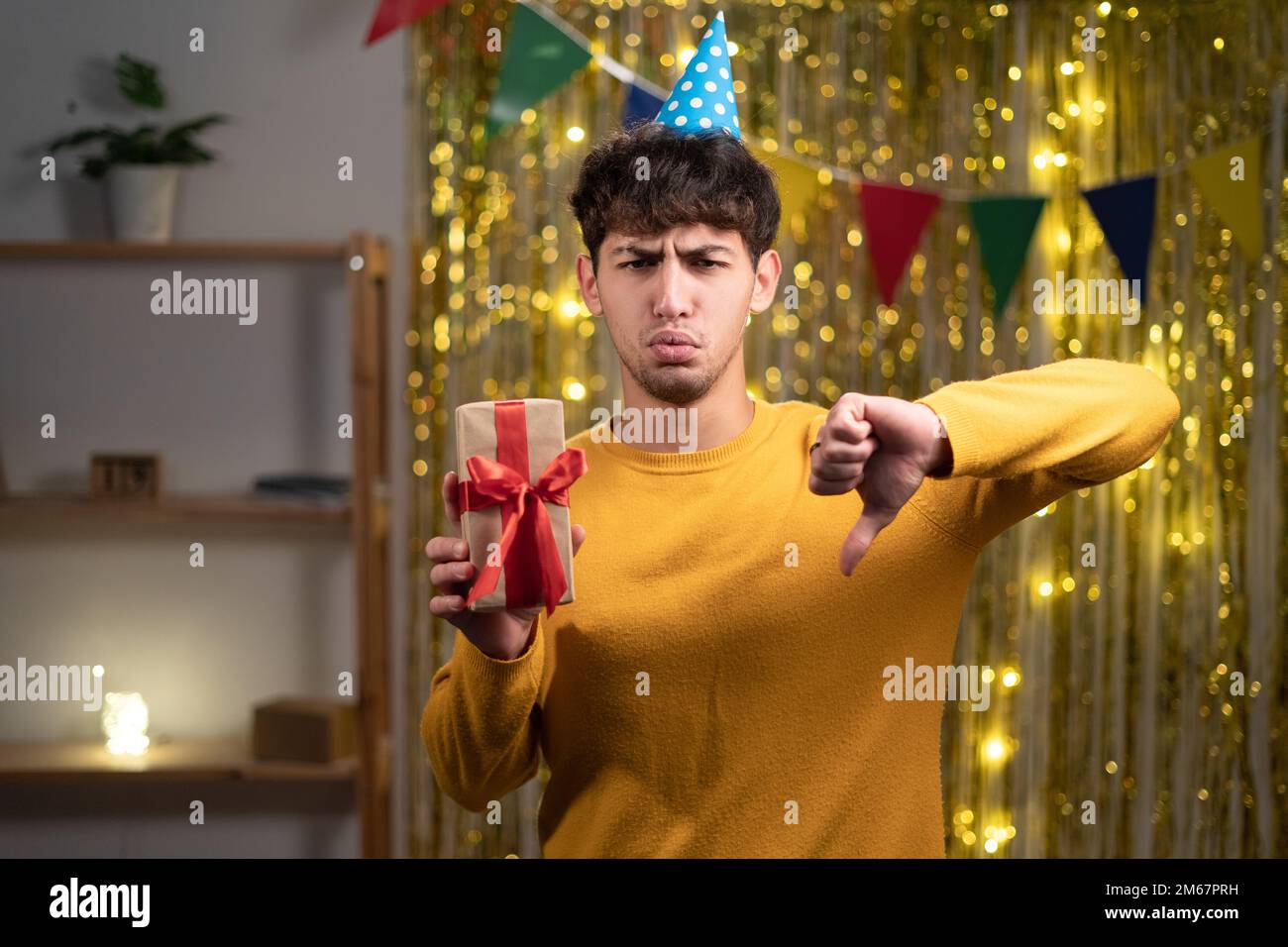 Young man holding present with angry face, negative sign showing dislike with thumbs down, rejection concept Stock Photo