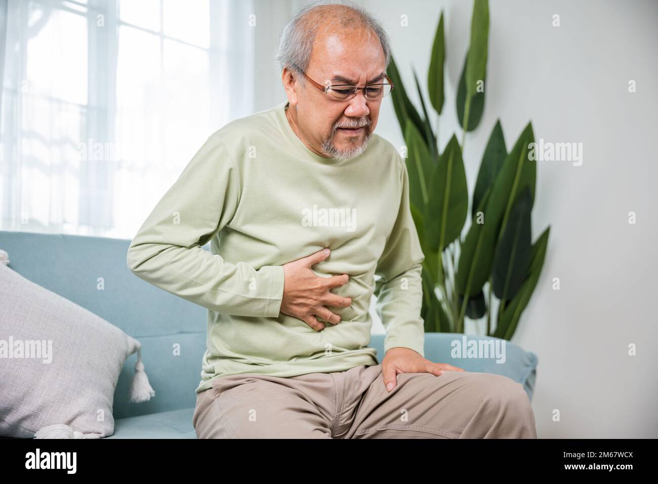 Senior Asian man sitting on sofa having suffering from stomach ache