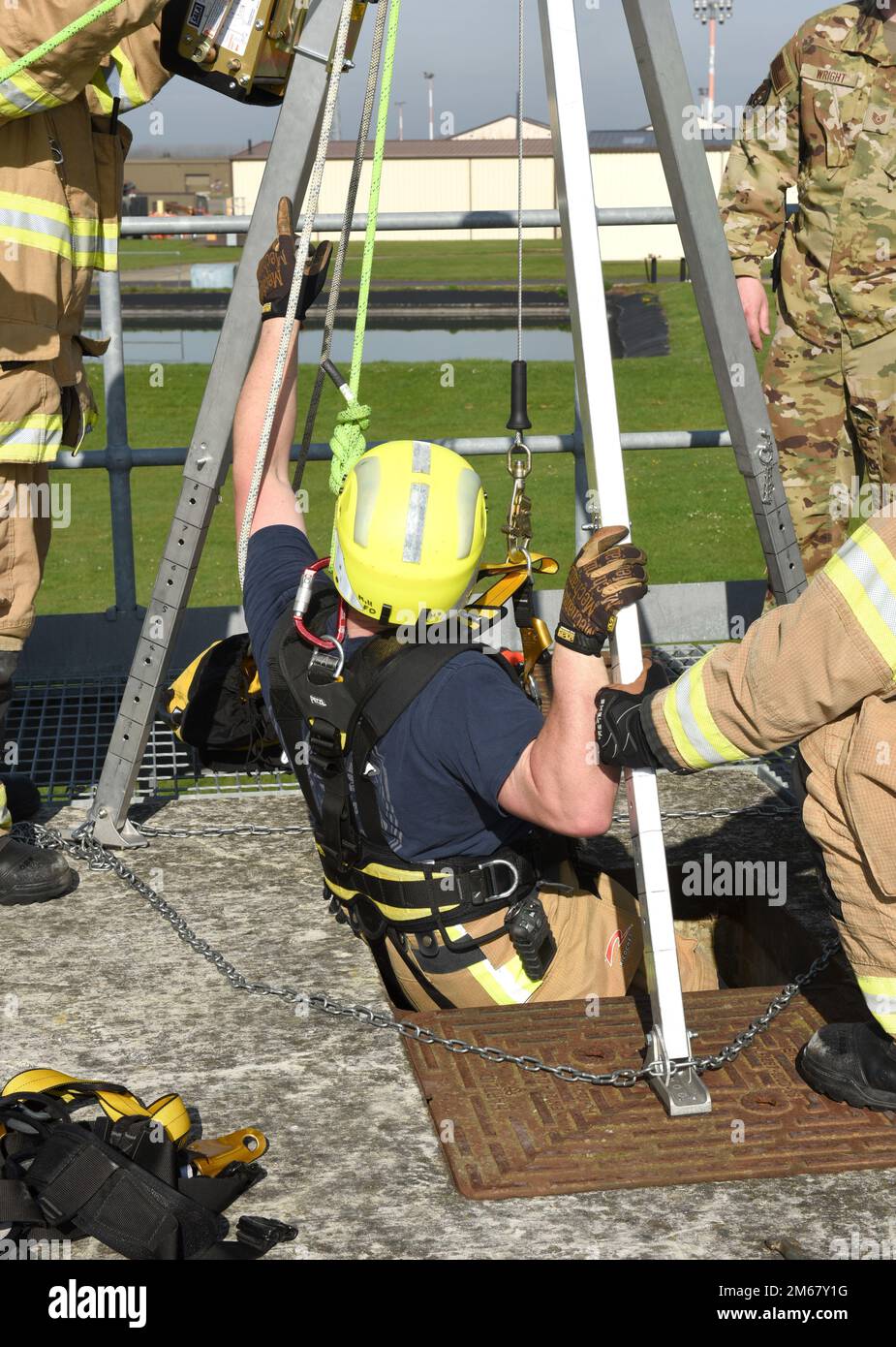 Firefighter Eddie Brant, 100th Civil Engineer Squadron Fire Department, rappels down into a confined space as other firefighters ensure he is securely attached and safe, during a training exercise at Royal Air Force Mildenhall, England, April 14, 2022. The scenario involved a teenager (simulated by a mannequin) who fell and was injured after climbing down into a facility. While climbing down to rescue the victim, another firefighter simulated also falling after slipping on a broken step, so Brant had to complete the rescue. Stock Photo