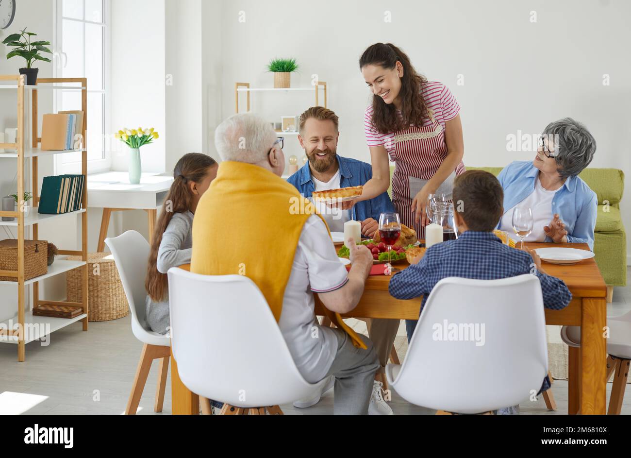 Woman serve the table for a large family in the dining room with a smile on her face. Stock Photo