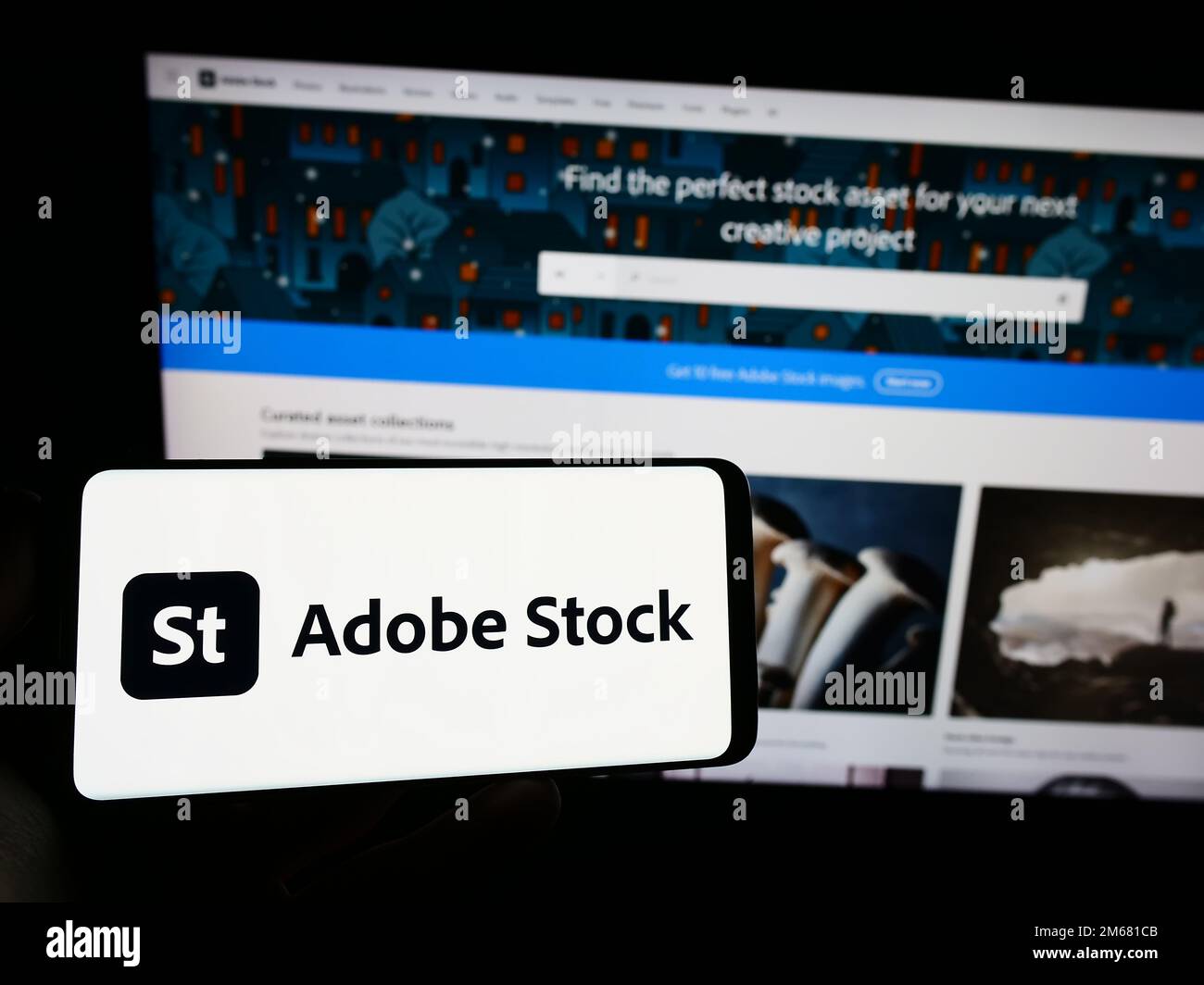 Person holding smartphone with logo of US microstock agency Adobe Stock on screen in front of website. Focus on phone display. Stock Photo