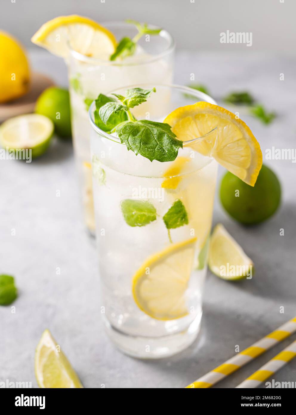 Lemonade drink with fresh lemons. Refreshing cocktail with lime, lemon, mint and ice in a tall glass on gray background close up. Summer cold drinks c Stock Photo