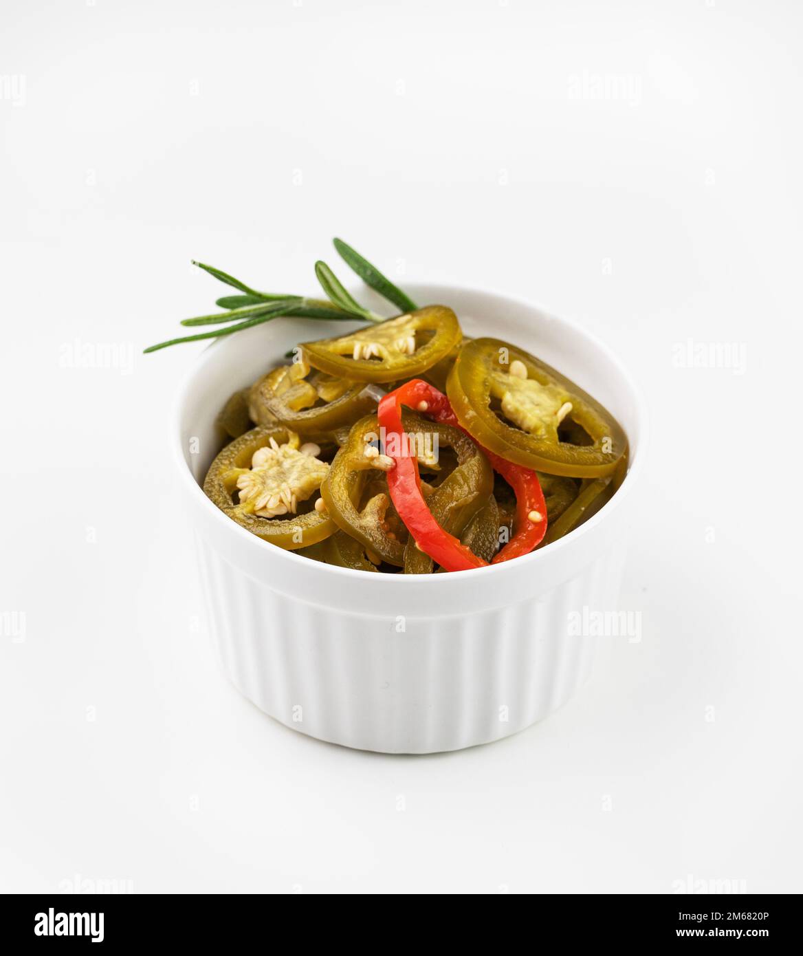 Hot jalapeno peppers sliced in a white bowl  with rosemary on isolated background. Traditional mexican vegetable snack. Stock Photo