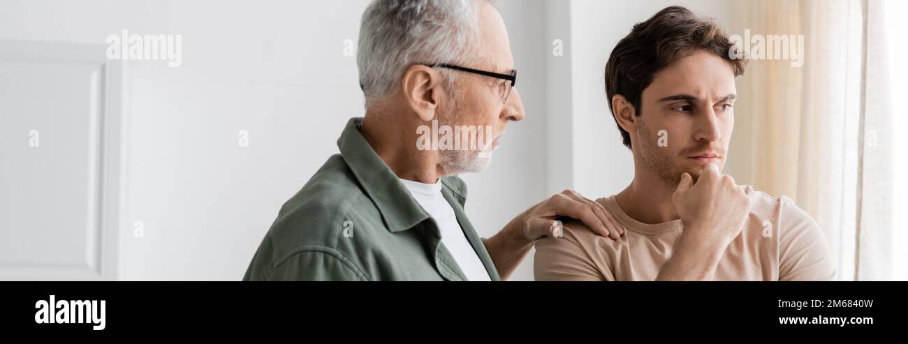 senior man touching shoulder of thoughtful and upset son standing with hand near face, banner,stock image Stock Photo