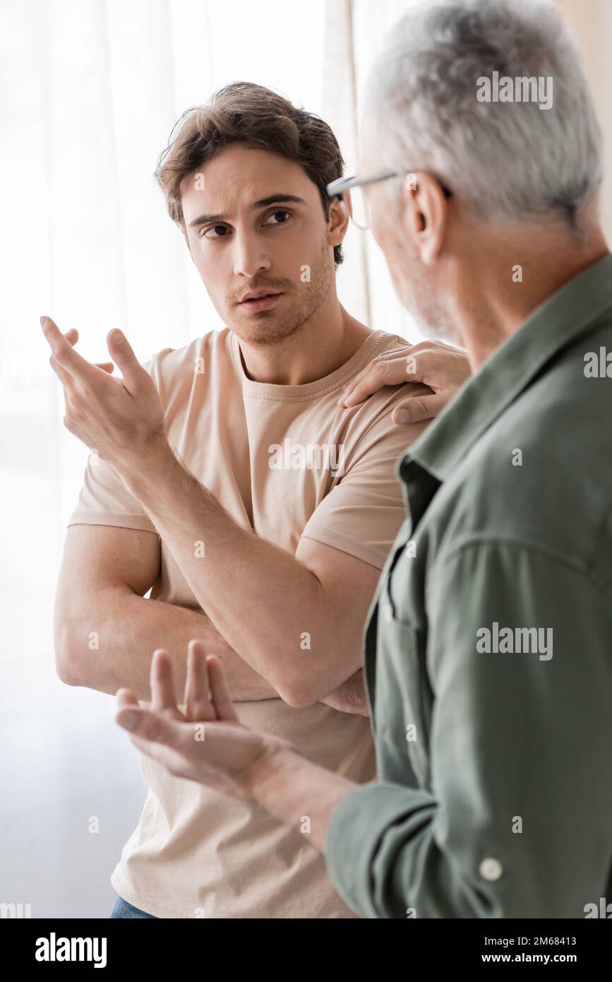 mature man touching shoulder and talking to upset son on blurred foreground,stock image Stock Photo