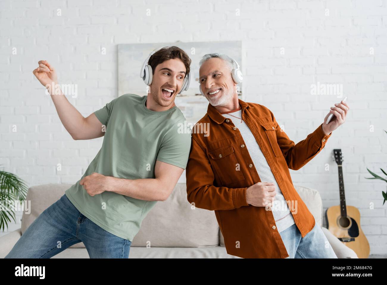 excited guy in wireless headphones singing and dancing with mature and cheerful dad at home,stock image Stock Photo