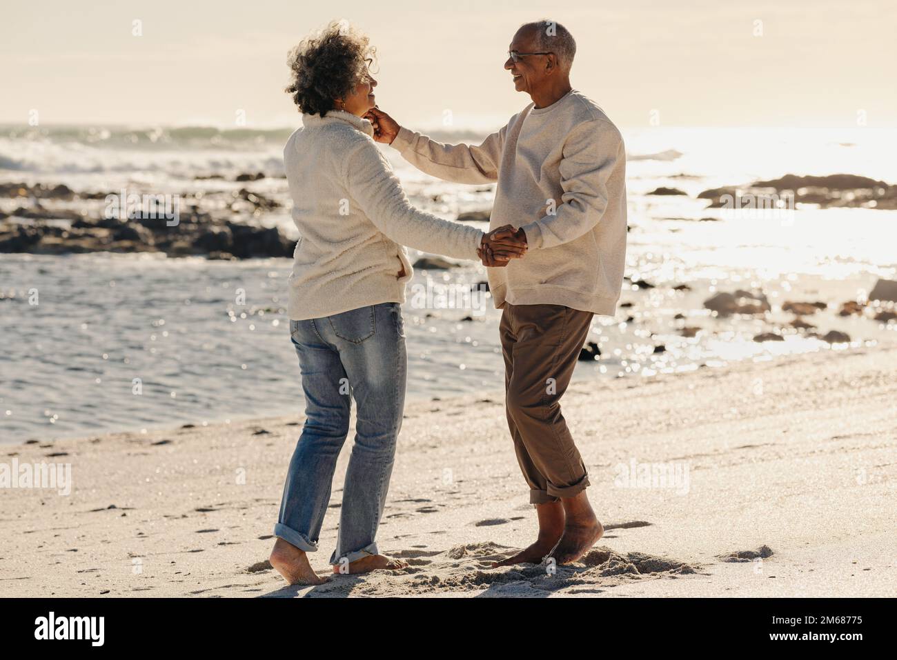 Happy elderly couple smiling and dancing together on beach sand. Mature couple having a good time next to the ocean. Cheerful senior couple enjoying t Stock Photo