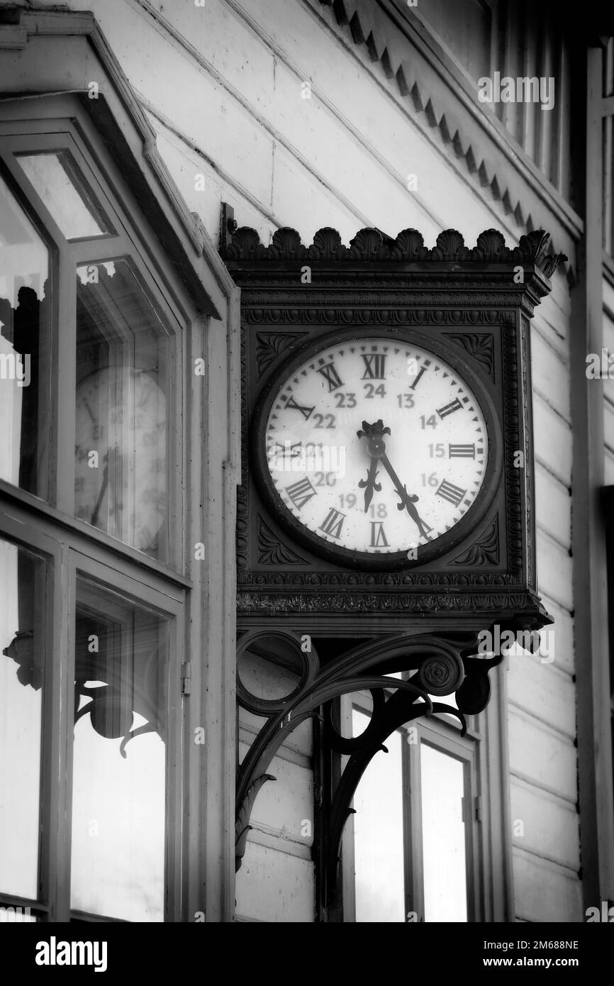 Old, nostalgic outdoor wall clock at railway station, vertical view. Monochrome conversion. Stock Photo