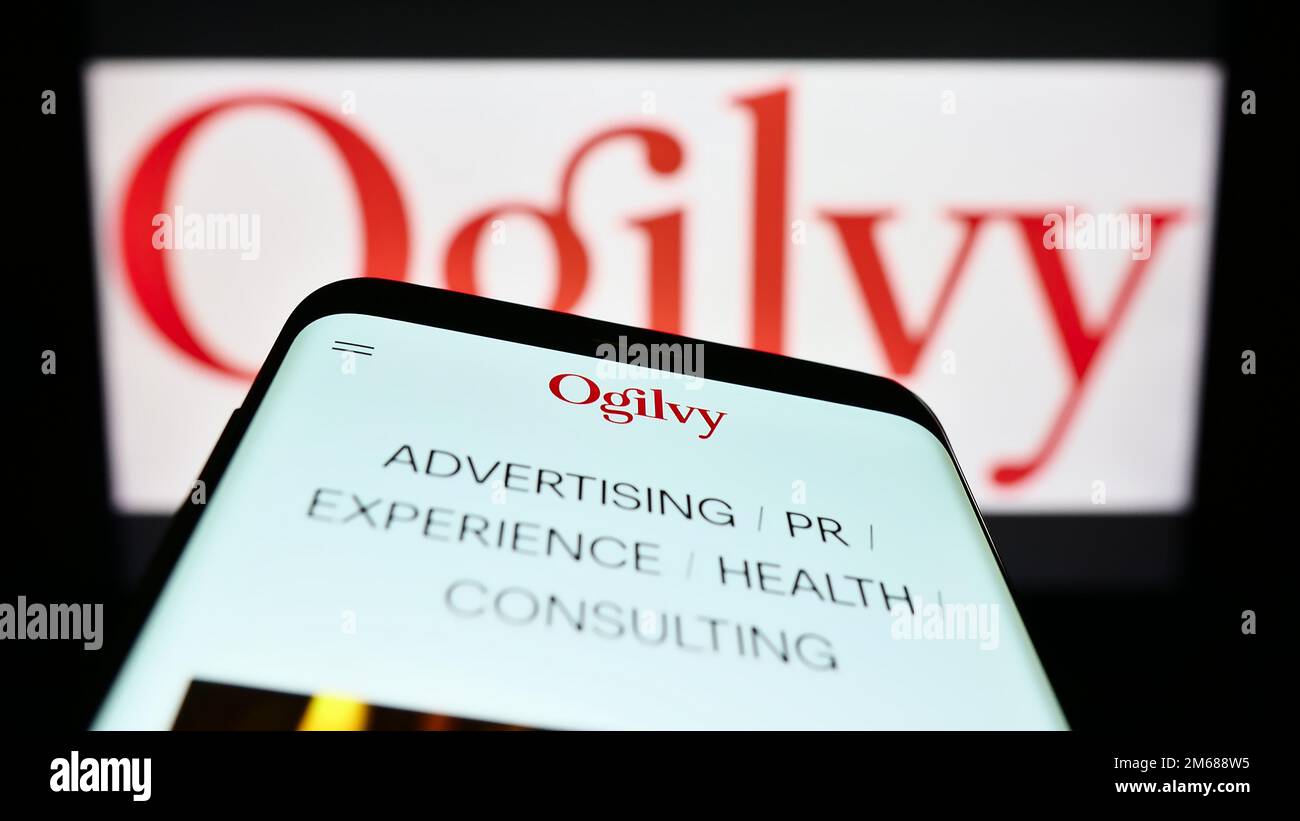 Mobile phone with website of advertising company Ogilvy on screen in front of business logo. Focus on top-left of phone display. Stock Photo