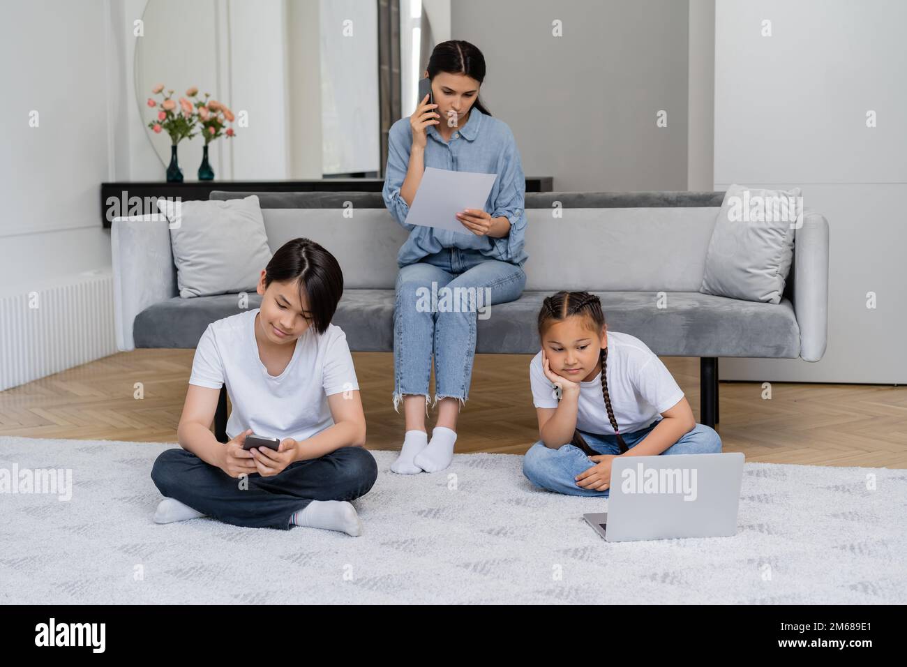 Asian children using devices while mother talking on smartphone and holding paper at home,stock image Stock Photo