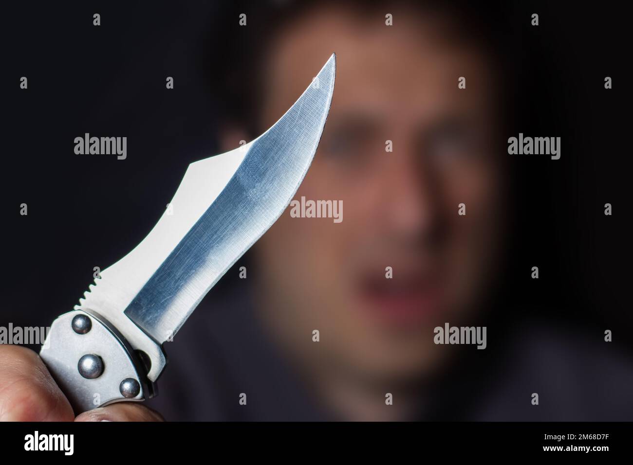 Close up of Hand with knife following young terrified man Bandit is holding a knife in hand. Threat Concept. Stock Photo