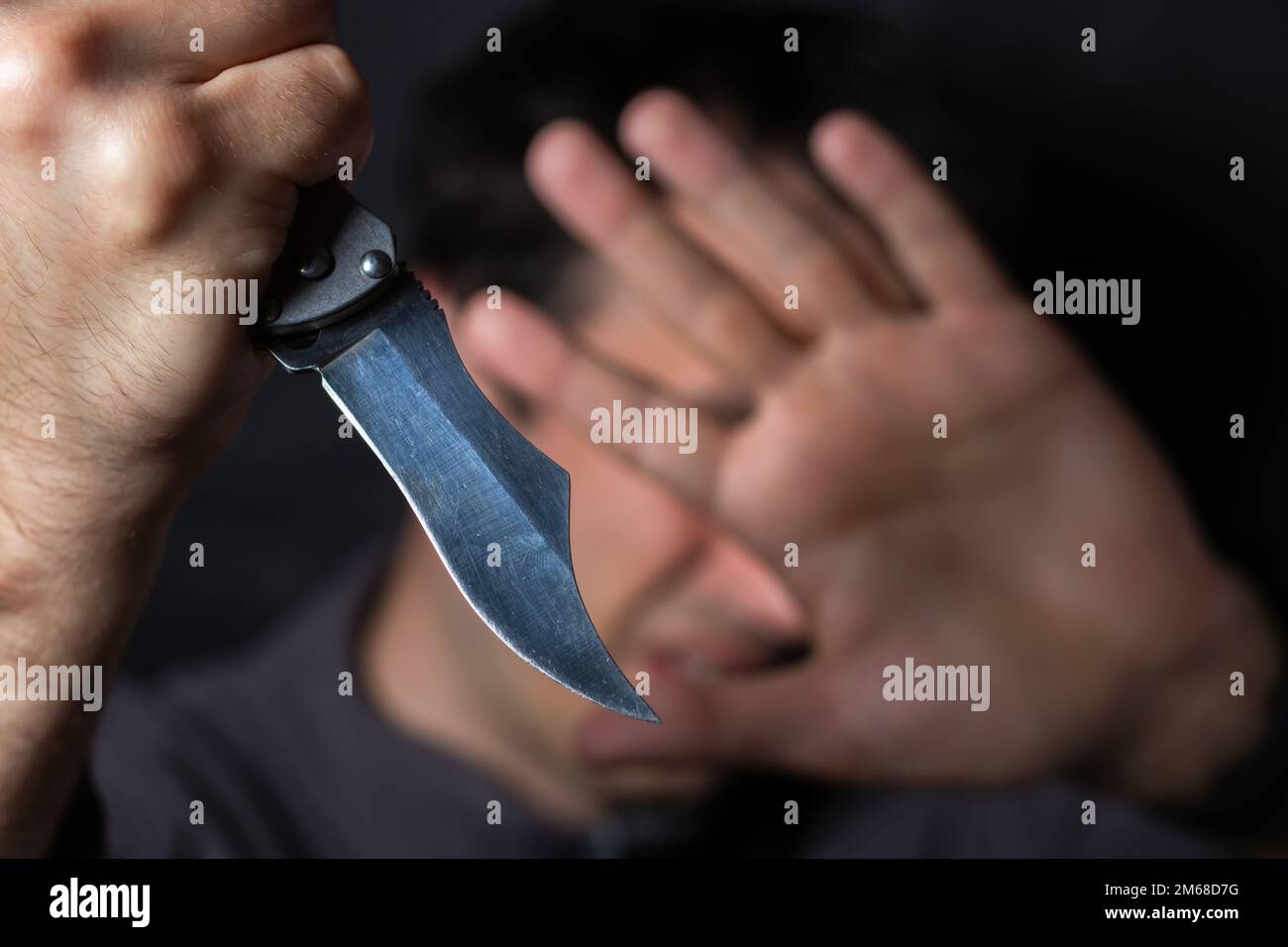 Close up of Hand with knife following young terrified man Bandit is holding a knife in hand. Threat Concept. Stock Photo