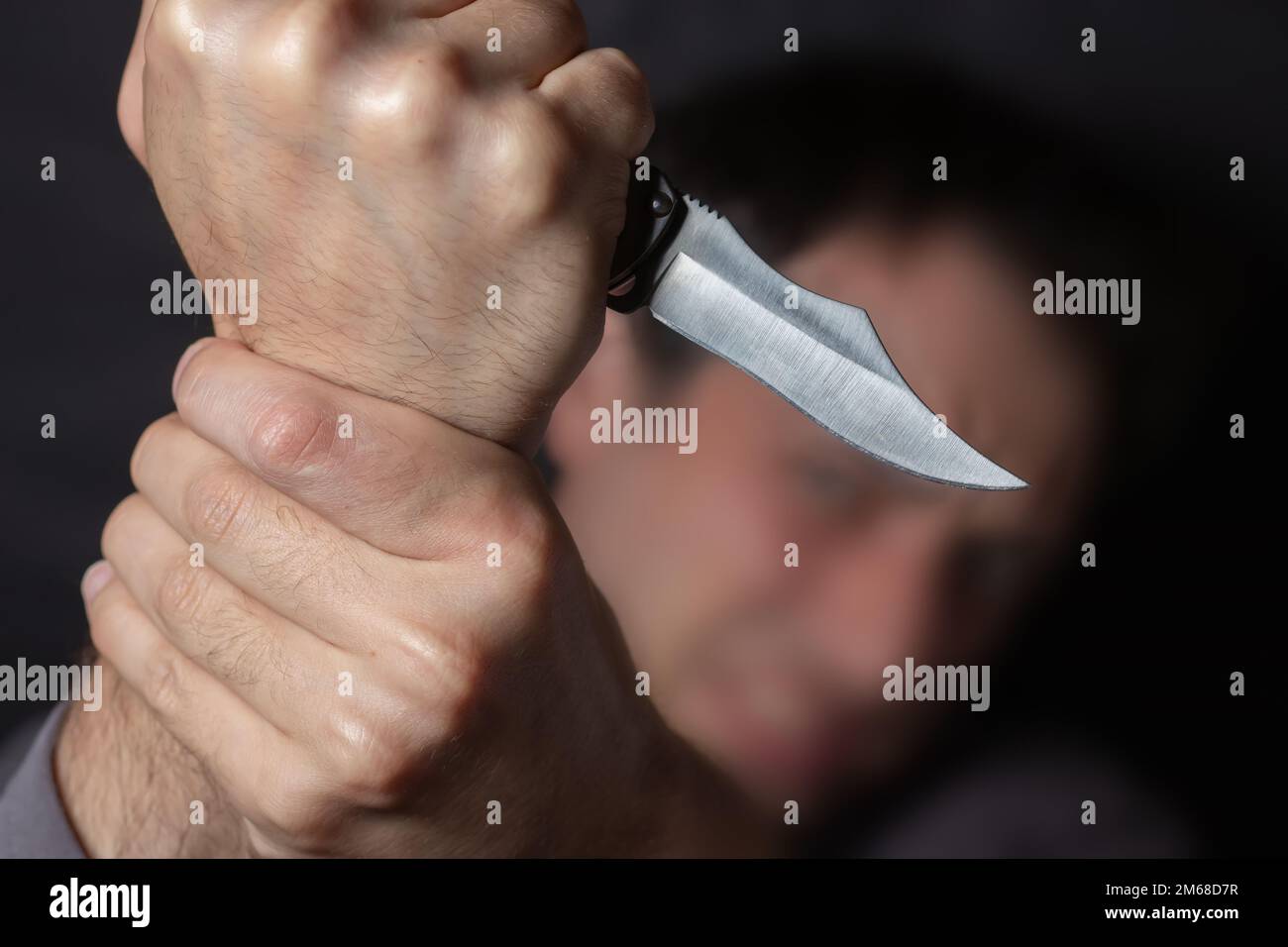 Close up of Hand with knife following young terrified man Bandit is holding a knife in hand. Threat Concept. Stock Photo