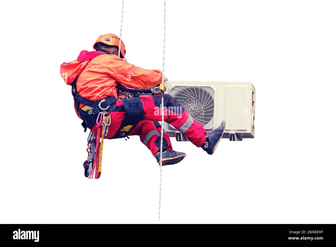 A male worker in a red uniform installs an air conditioner in a niche under the window, isolated on a white background Stock Photo